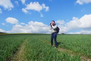Young woman standing in field, taking photograph of landscape