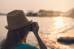 Young woman traveler taking photo on the beach at beautiful sunset