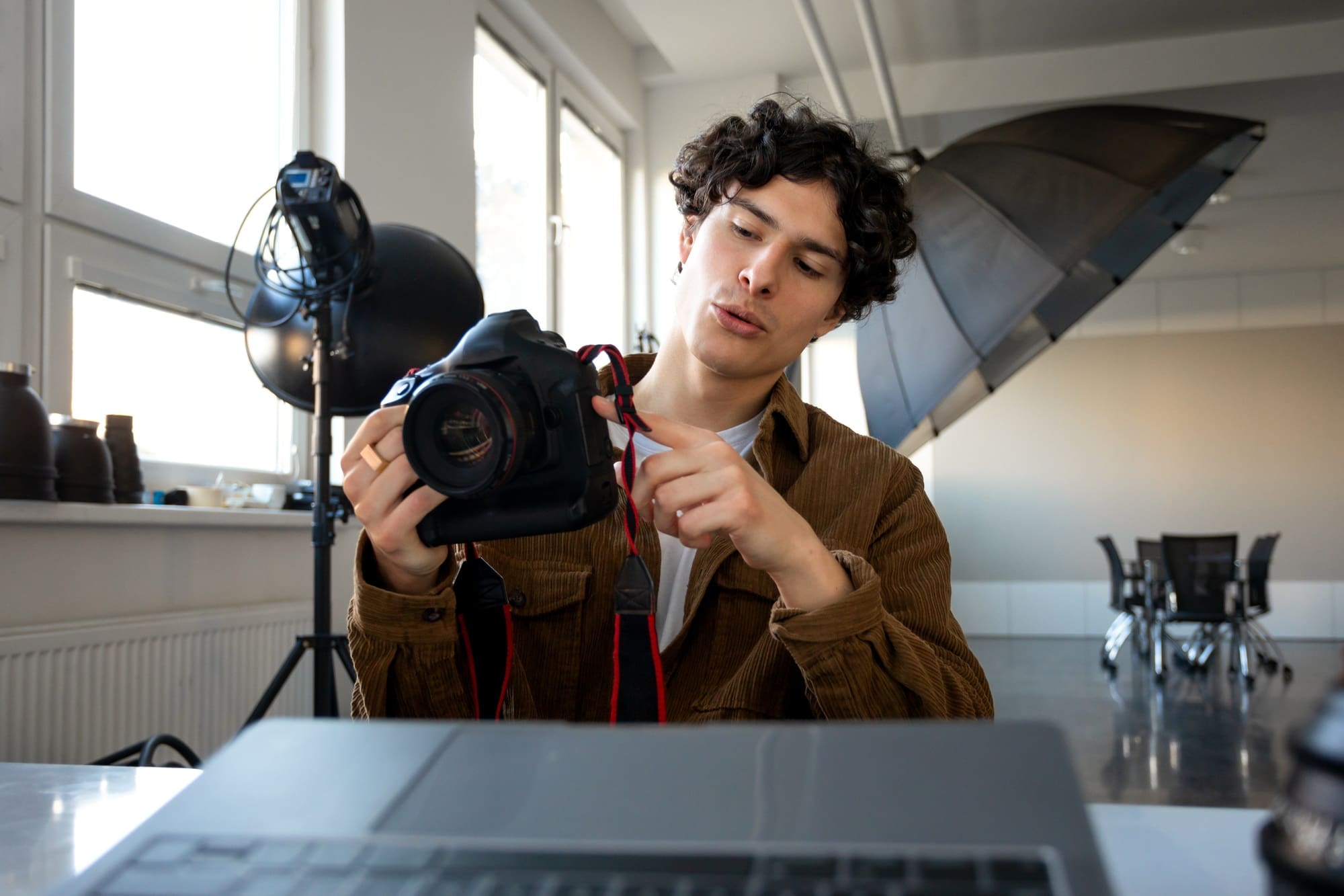 European male photographer using modern photo camera while working on laptop at workplace in studio