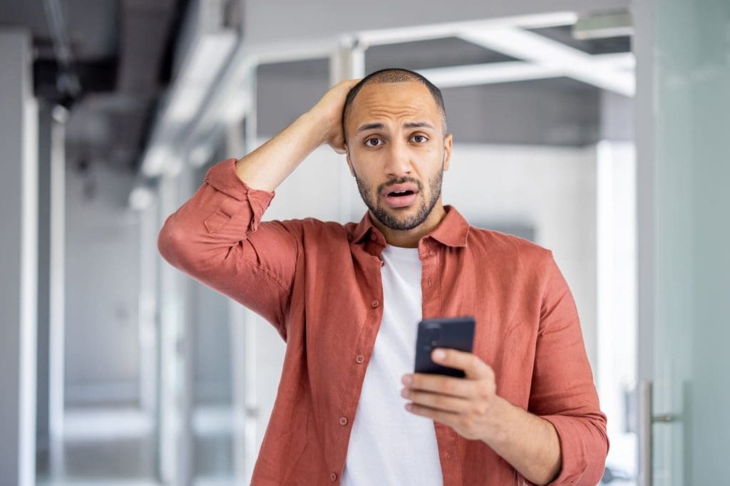 hombre sorprendido por recibir critica en telefono como mensaje agarrando su cabeza