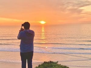 Person taking a photo using technology to capture a special sunset over the horizon, Pacific Ocean